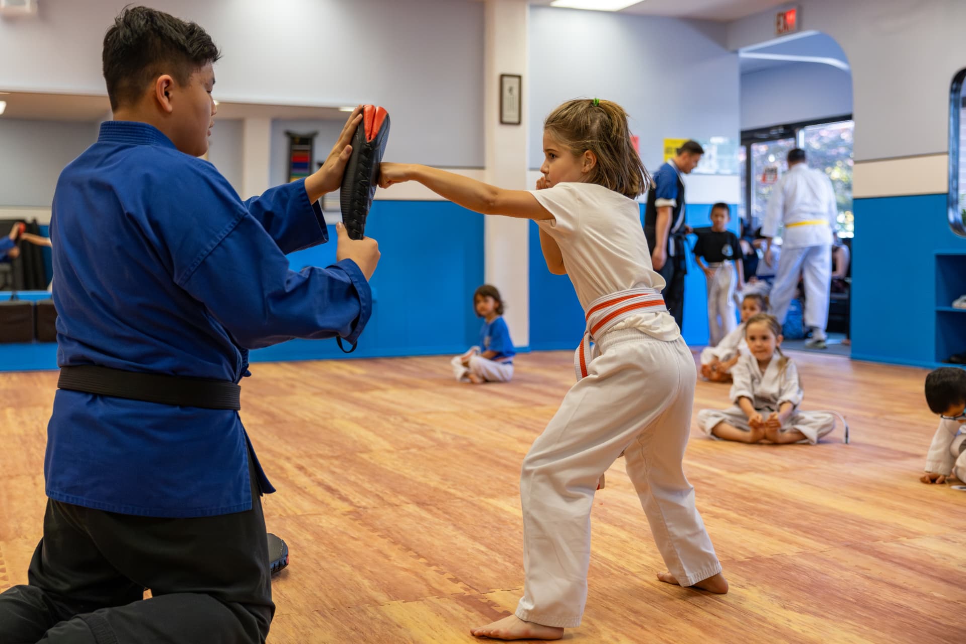 Young student punching a target pad held by an instructor